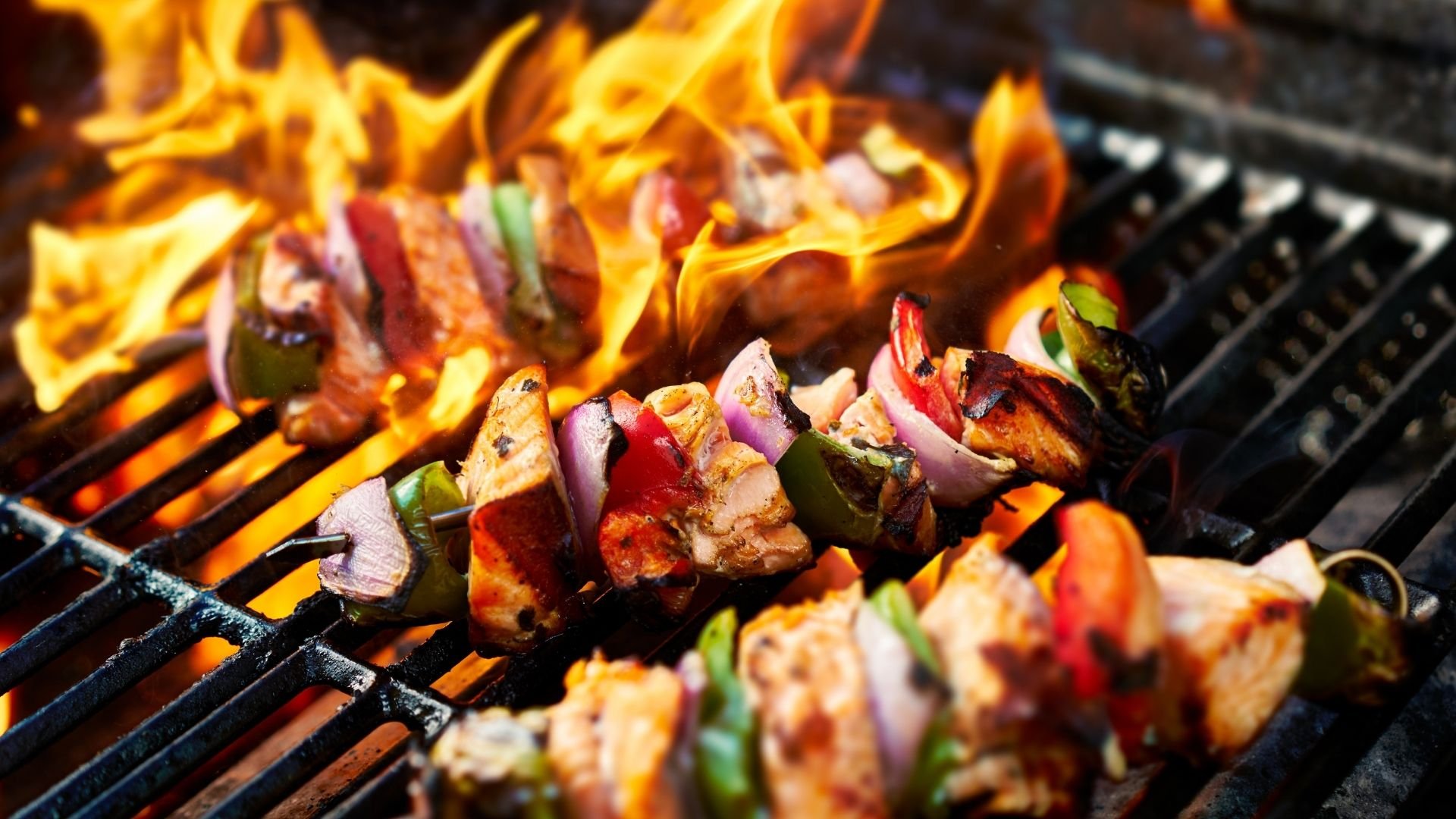 Colorful vegetable and meat kebabs grilling over open flames and coals on barbecue.