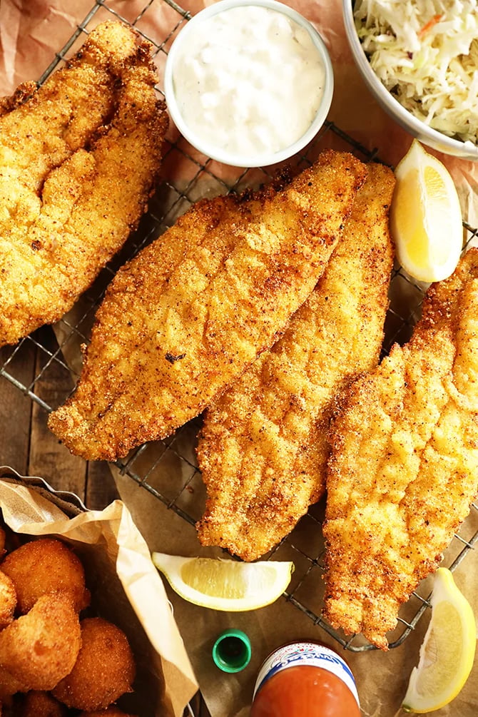 Crispy fried fish fillets on wire rack with tartar sauce, coleslaw, and lemon wedges