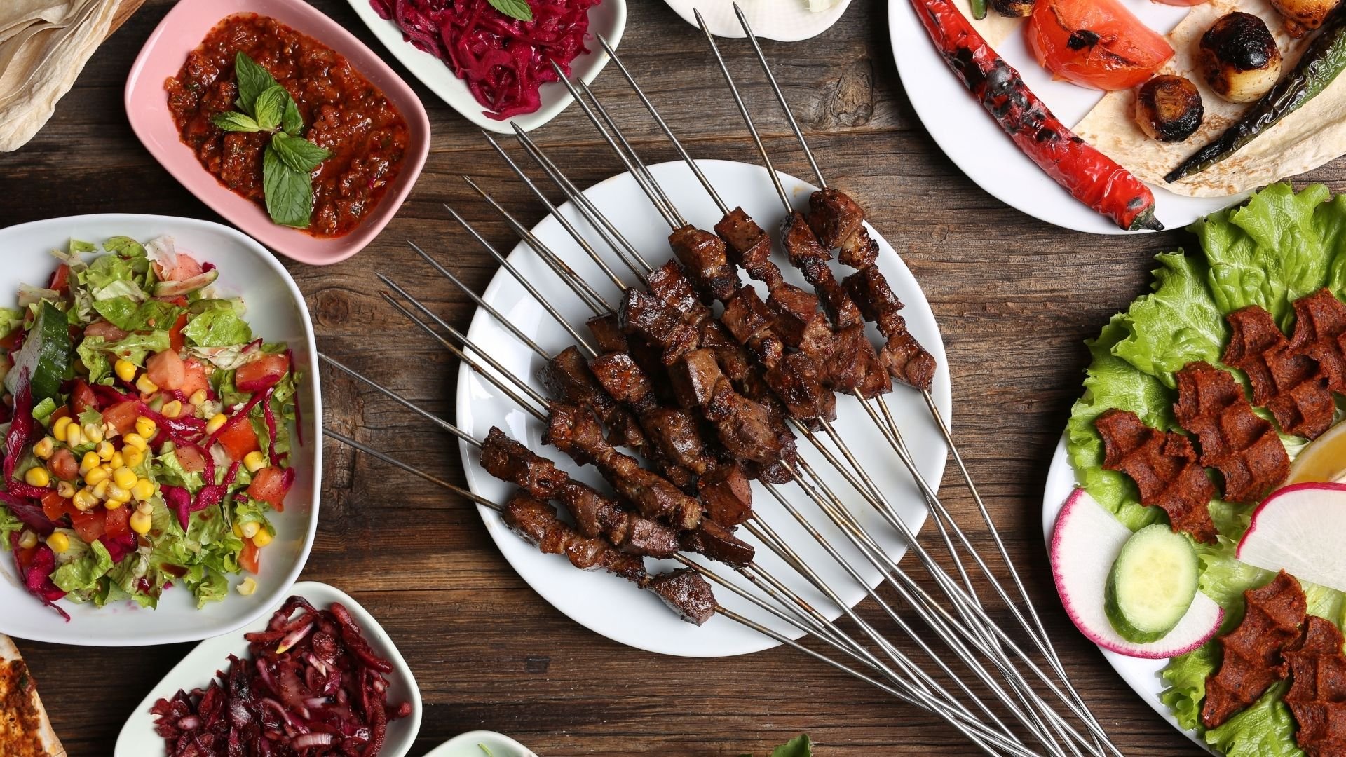 Overhead view of Middle Eastern mezze spread with meat skewers, grilled vegetables, salads, and dips