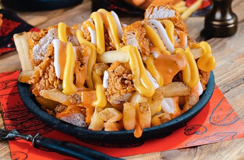 Fried chicken sandwich loaded with fries, mustard, and mayo on skillet plate