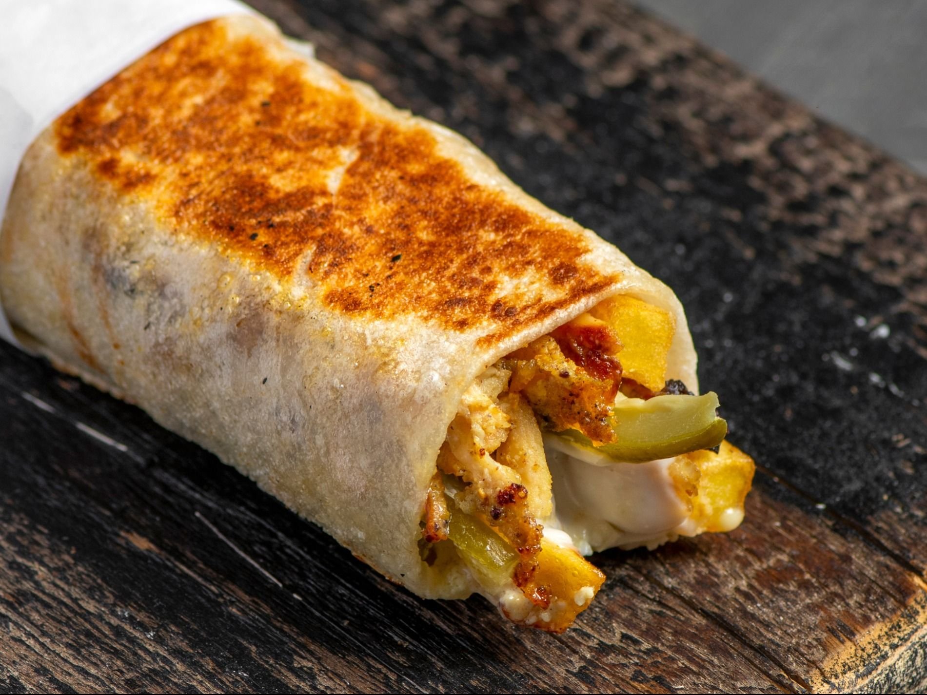 Golden burrito with cheese and vegetables on rustic wooden surface