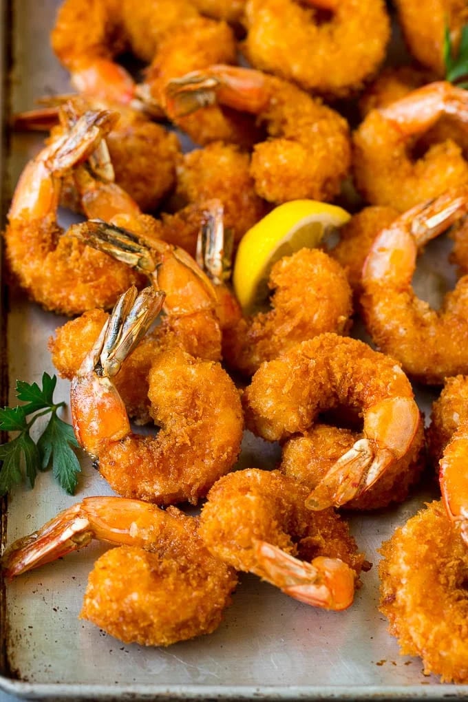 Golden fried shrimp with tails, lemon slice, and fresh parsley garnish on plate.